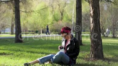 美丽年轻<strong>时尚</strong>的女人坐在公园的一棵树下，喝着一杯咖啡。 大自然中的外卖咖啡。 <strong>时尚时尚时尚</strong>